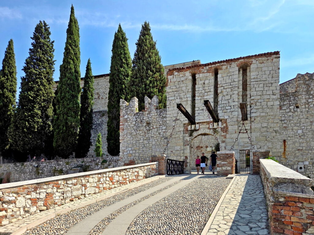 A stone bridge leading to a medieval gatehouse with drawbridge mechanisms at Brescia Castle.