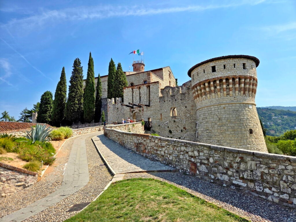 Brescia Castle walls and round tower along cobbled path, Italy