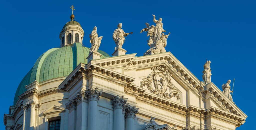 Sculpted figures atop the white marble facade of Duomo Nuovo cathedral in Brescia, Italy.