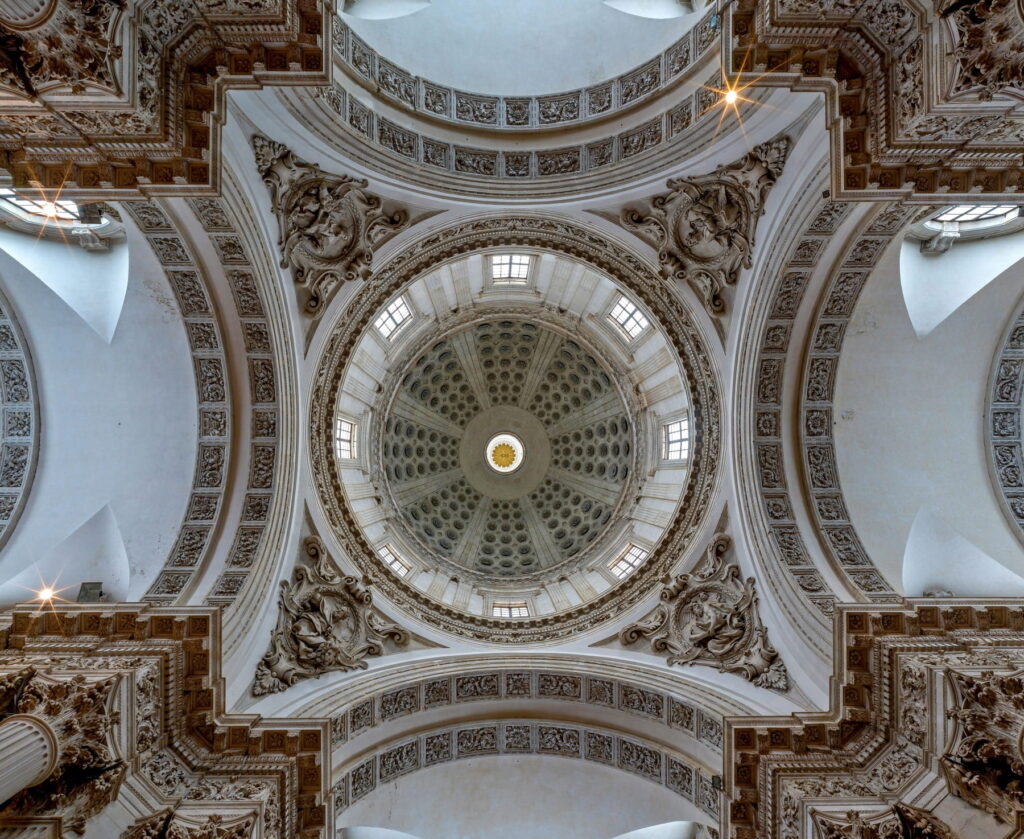 Symmetrical upward view of the ornate interior dome and vaulted ceiling of Duomo Nuovo, Brescia.