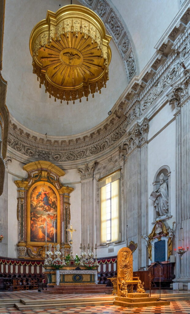 The main altar of Brescia Cathedral with a golden canopy and a large painting of the Assumption.