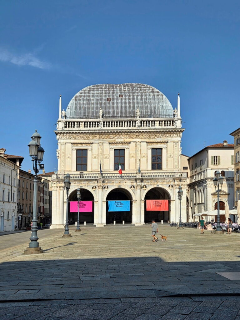 Front view of the white marble Palazzo della Loggia with colorful banners under its arches in Brescia, Italy.