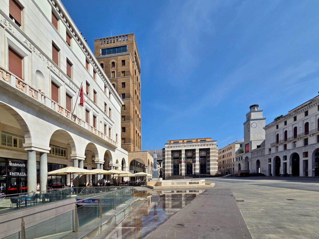 The reflection of Rationalist buildings in a shallow pool in Piazza della Vittoria, Brescia.