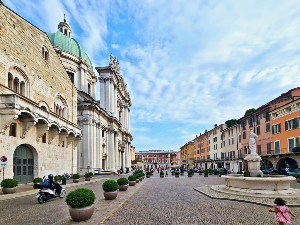 Wide view of Piazza Paolo VI showing the massive white Duomo Nuovo cathedral and the Minerva fountain.