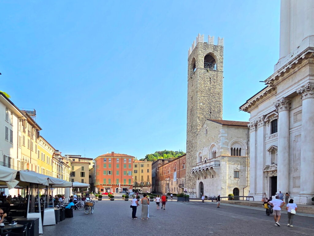 The medieval stone tower of the Broletto palace overlooking a wide pedestrian square in Brescia.