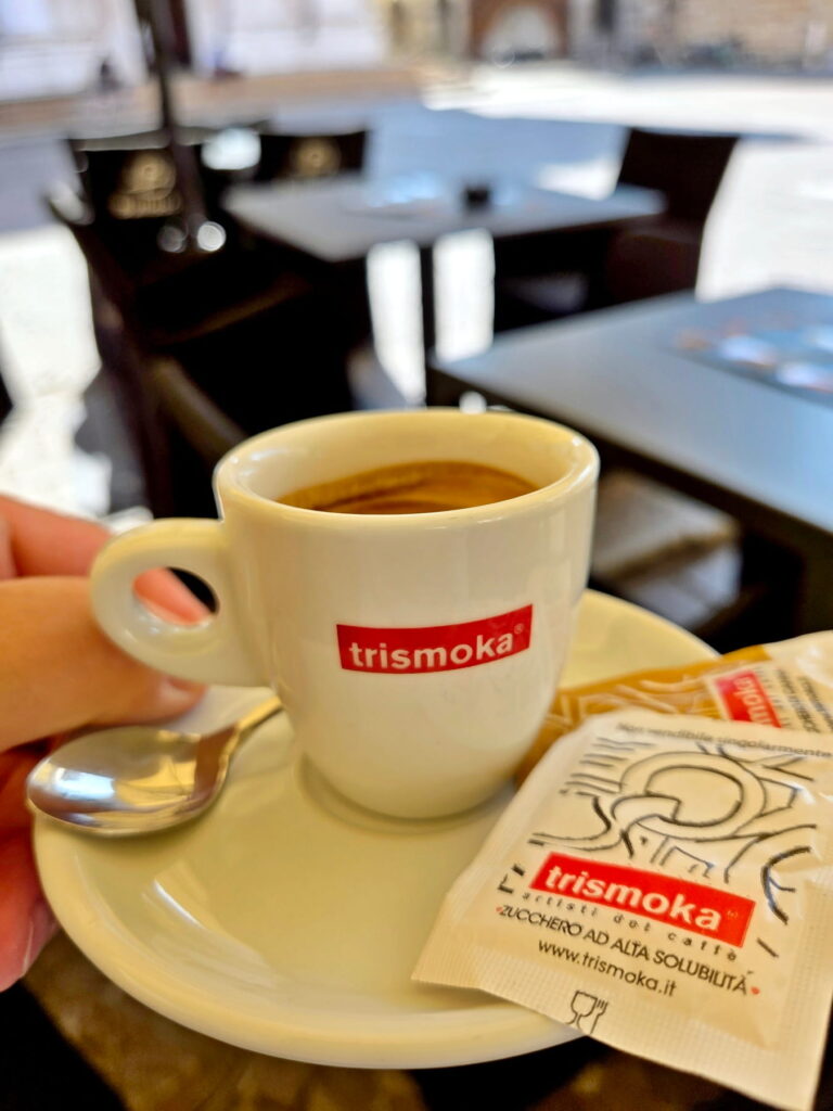 A close-up of a white cup of Italian espresso on a saucer at an outdoor cafe in Brescia.