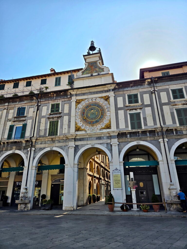 The astronomical clock tower with gold and blue details above an arched walkway in Brescia.