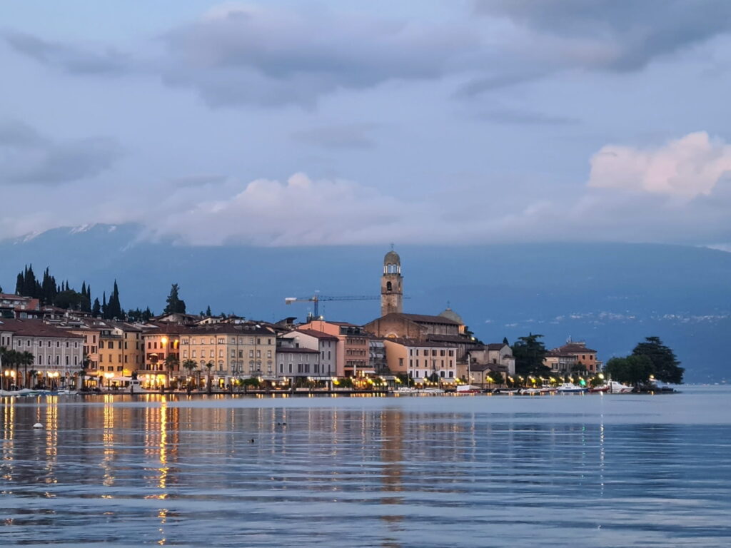Evening view of Salò waterfront in Italy with historic buildings and church tower reflected in Lake Garda.
