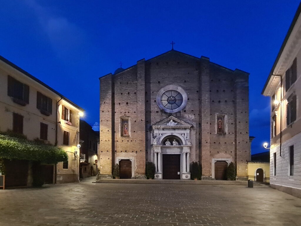 The brick facade of Salò Duomo illuminated at night on a quiet paved square in Italy.