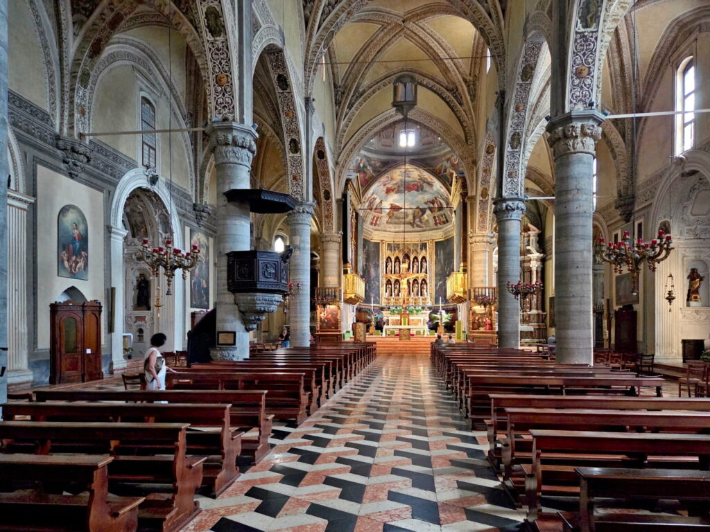 Interior of Salò Duomo showing the nave, marble pillars, and a distinctive 3D-effect geometric tiled floor.