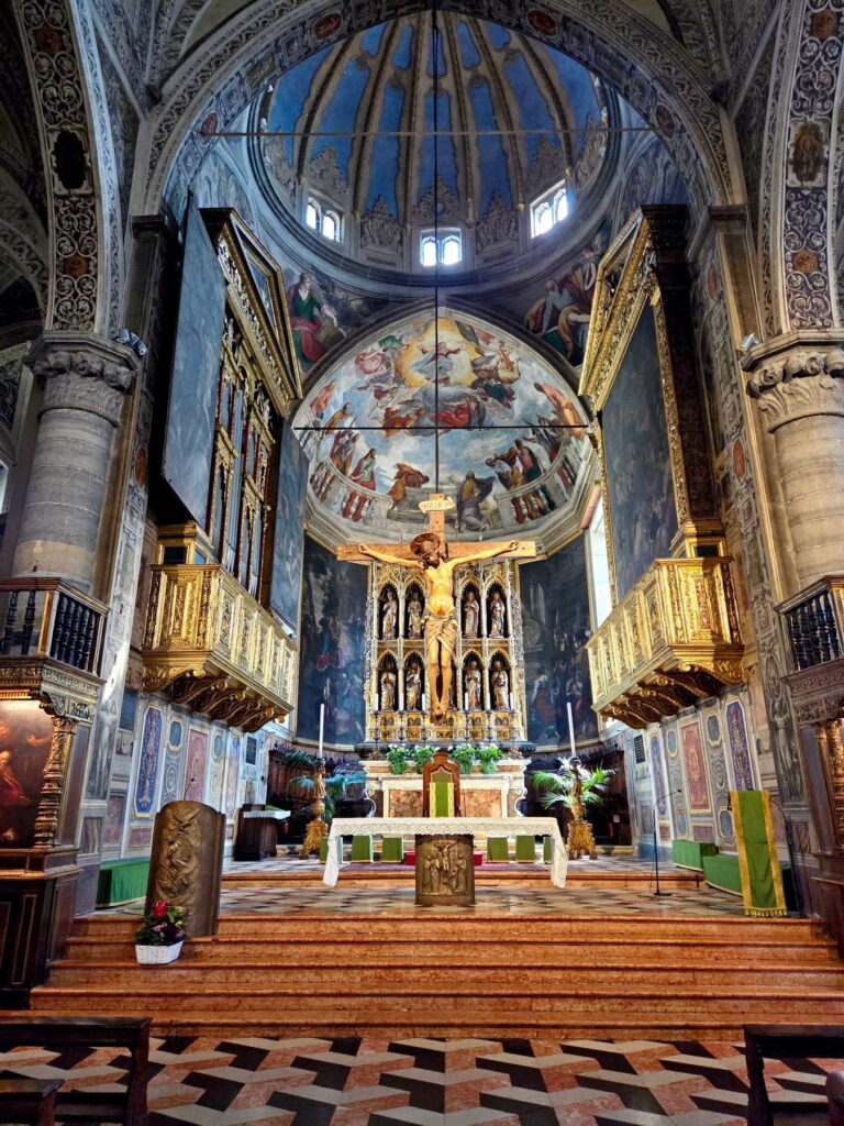The main altar of Salò Duomo featuring a large wooden crucifix and vibrant frescoed dome.
