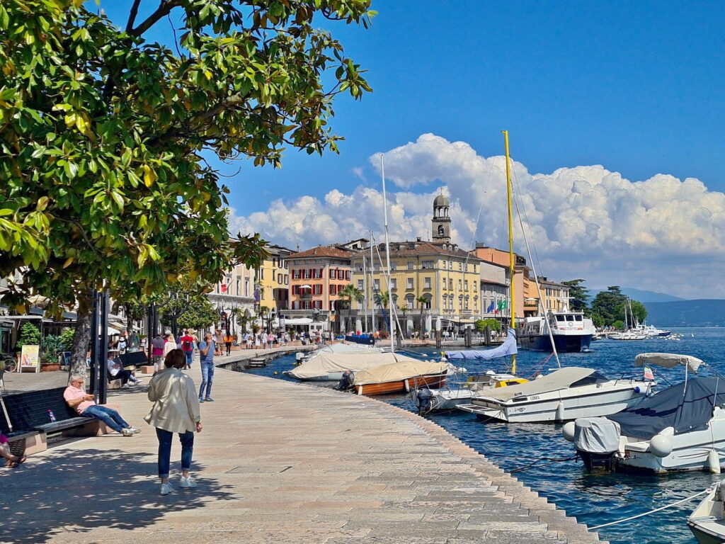 Sunny lakeside promenade in Salò, Italy, with moored boats, historic buildings, and the Lake Garda shoreline.