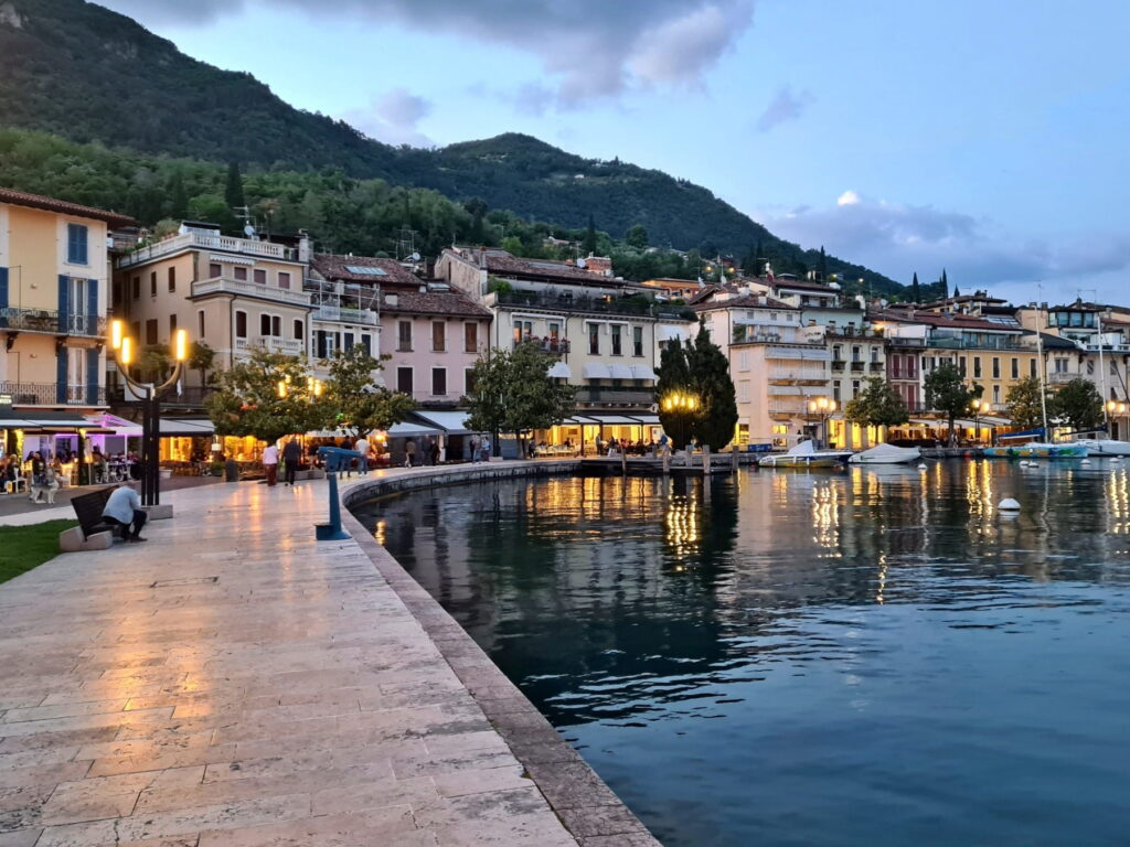 Evening view of the curved Salò promenade with warm streetlights reflecting on the calm surface of Lake Garda.