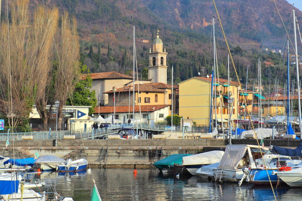 Boats in the Salò marina with a church bell tower and green hills in the background at Lake Garda, Italy.