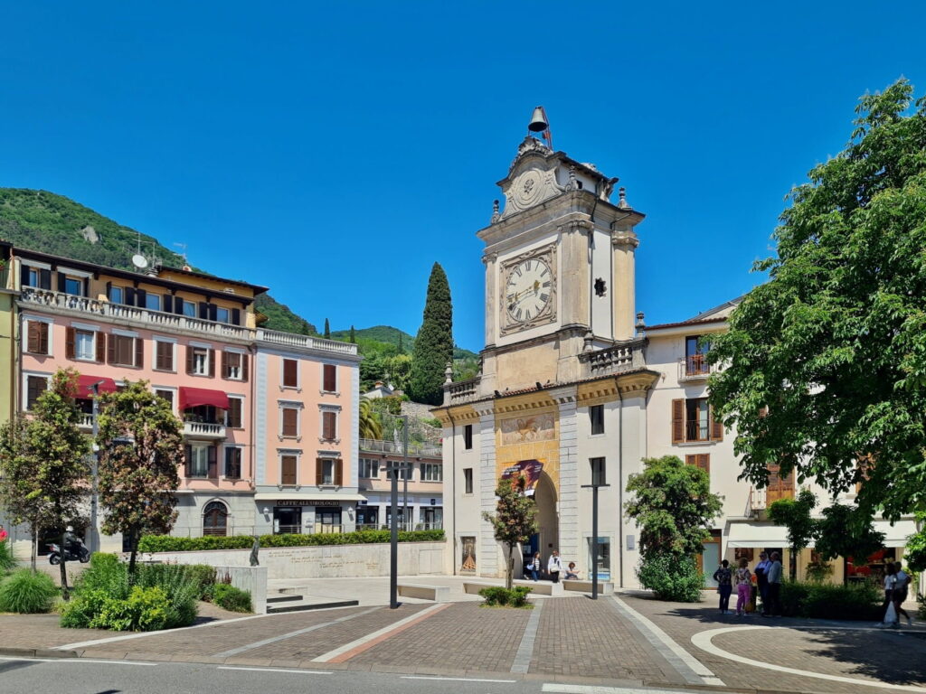 The historic Torre dell'Orologio gatehouse in Salò, Italy, standing in a sunny square surrounded by colorful buildings.