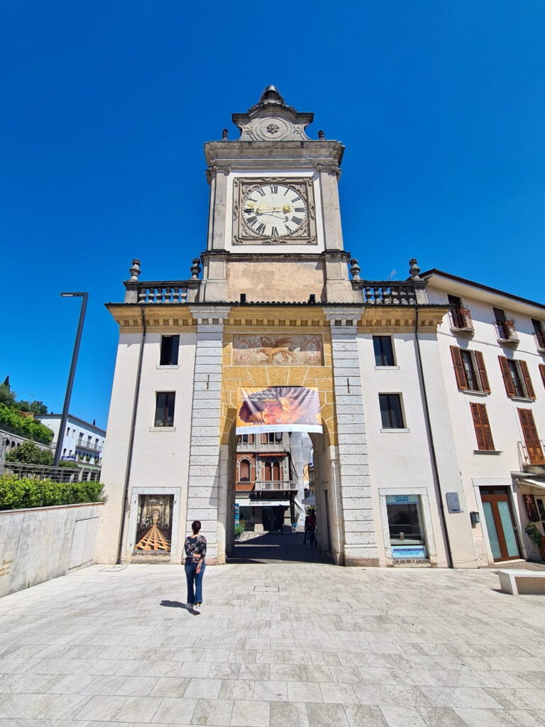 Front view of the Torre dell'Orologio clock tower in Salò with a winged lion fresco above the archway.