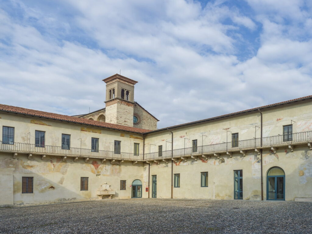 A large cobblestone courtyard surrounded by historic monastic buildings at the Santa Giulia Museum in Brescia.