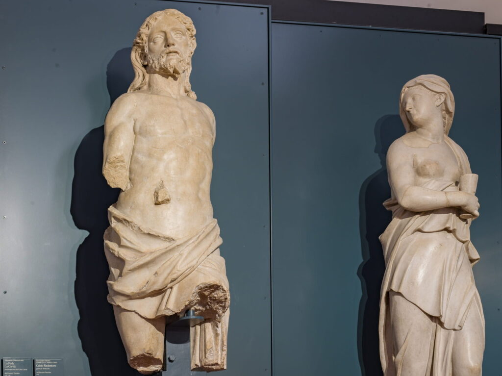 Ancient marble statues of religious figures displayed against a dark gray background in a museum gallery.